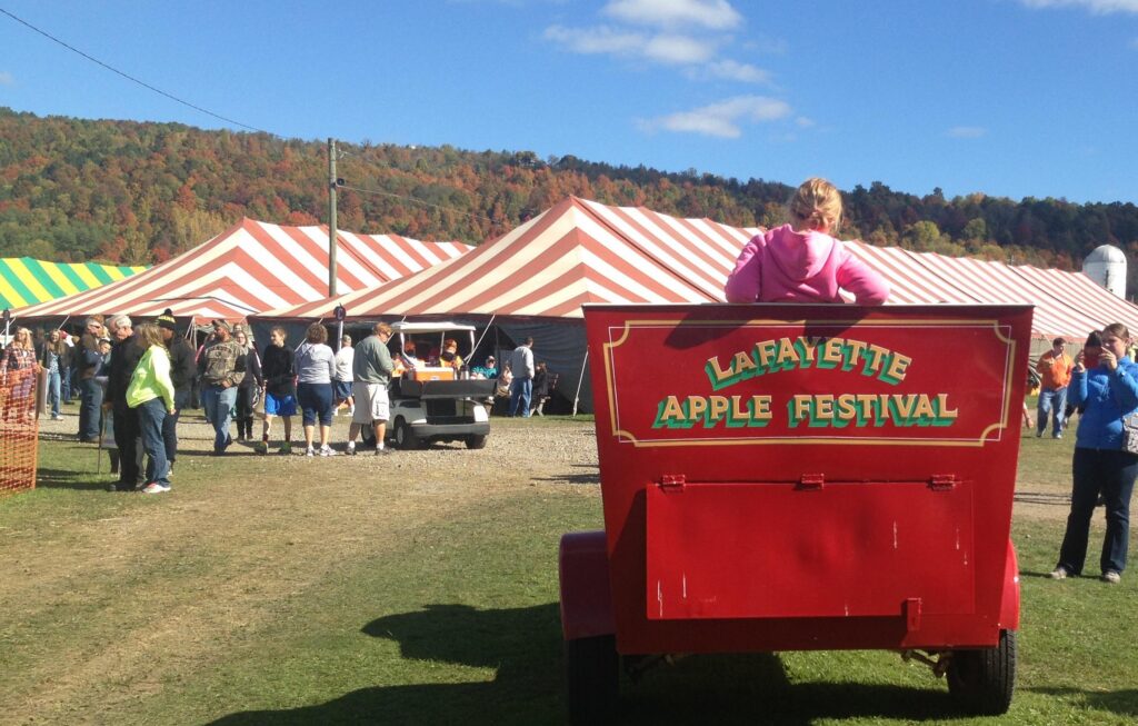 Lafayette Apple Festival sign with festival tents and guests during fall near Skaneateles, New York.
